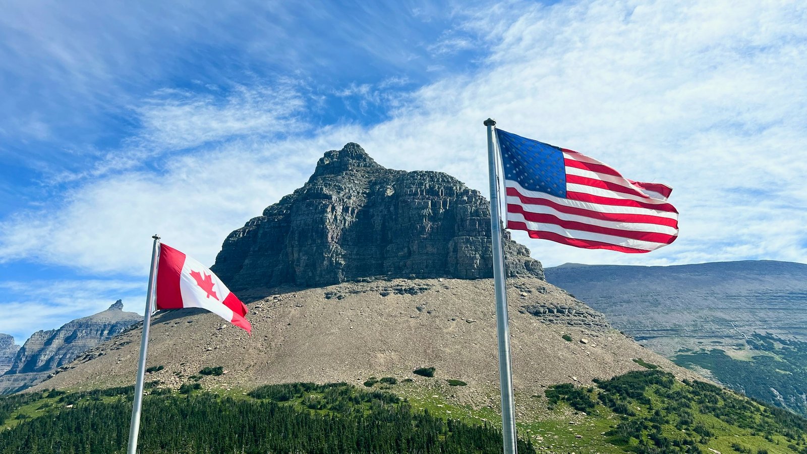 USA and Canada flags near mountain peak.